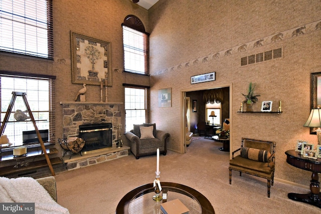 carpeted living area featuring a towering ceiling, a stone fireplace, and visible vents