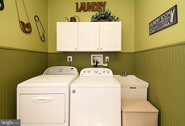 clothes washing area with independent washer and dryer, a sink, a wainscoted wall, and cabinet space