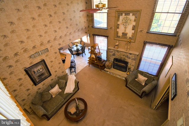 living room featuring a towering ceiling, wallpapered walls, a fireplace, carpet flooring, and a ceiling fan