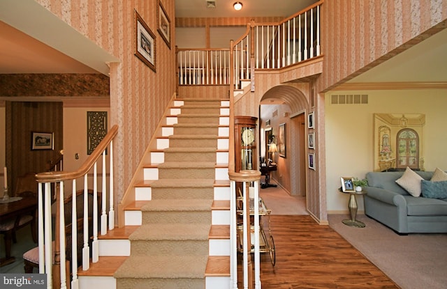 stairs with baseboards, wallpapered walls, a towering ceiling, and visible vents