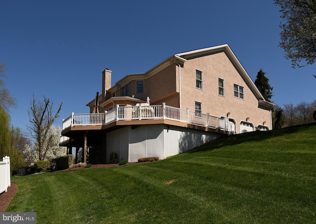 back of property with a chimney, a deck, a lawn, and stucco siding