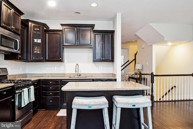 kitchen with a sink, dark wood-style flooring, appliances with stainless steel finishes, a kitchen bar, and light stone counters