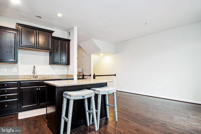 kitchen with a kitchen island, light stone countertops, dark wood-type flooring, a breakfast bar area, and a sink