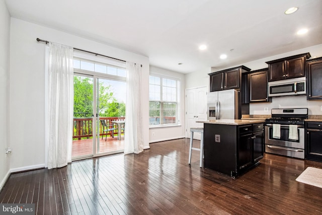 kitchen with a breakfast bar, baseboards, a kitchen island, dark wood finished floors, and stainless steel appliances