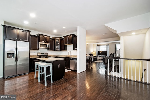 kitchen with dark wood finished floors, dark brown cabinets, a kitchen island, appliances with stainless steel finishes, and a sink