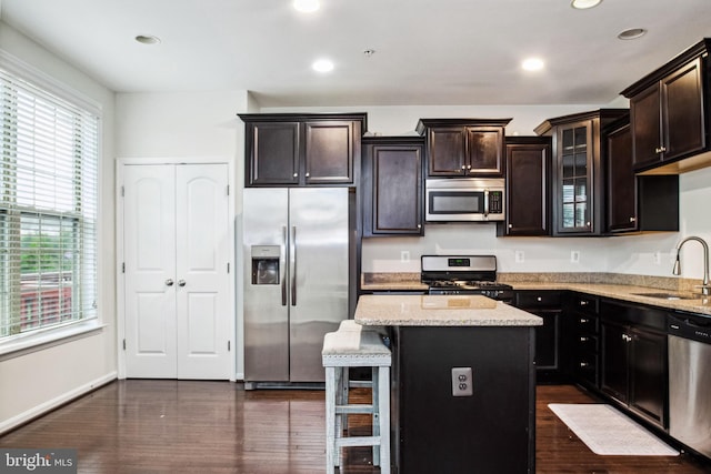 kitchen with glass insert cabinets, a sink, dark wood-style floors, stainless steel appliances, and light stone counters