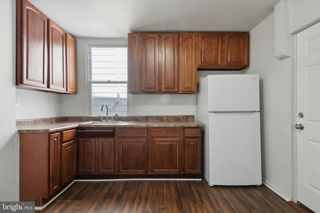 kitchen featuring a sink, freestanding refrigerator, dark countertops, dark wood finished floors, and brown cabinets