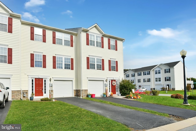 townhome / multi-family property featuring a front lawn, driveway, stone siding, and an attached garage