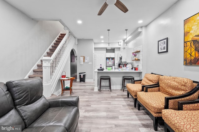 living room featuring arched walkways, light wood-type flooring, a ceiling fan, recessed lighting, and stairs