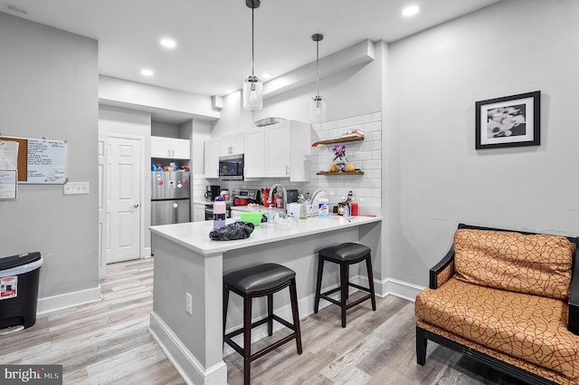 kitchen featuring a peninsula, backsplash, white cabinets, a kitchen bar, and appliances with stainless steel finishes