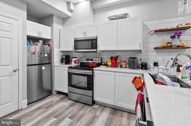 kitchen with light wood-style flooring, backsplash, white cabinets, stainless steel appliances, and a sink