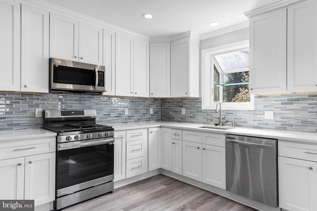 kitchen with a sink, light wood-type flooring, ornamental molding, white cabinets, and appliances with stainless steel finishes