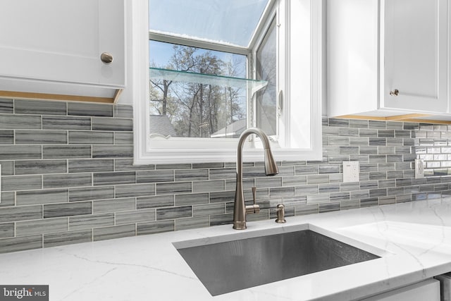 kitchen with backsplash, light stone countertops, a sink, and white cabinetry