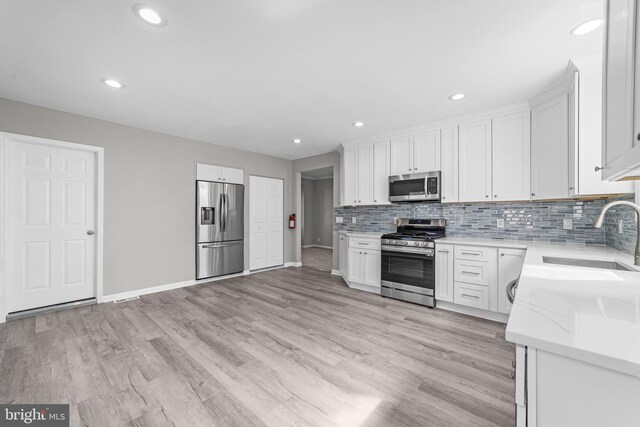 kitchen featuring a sink, stainless steel appliances, light wood-type flooring, backsplash, and white cabinets