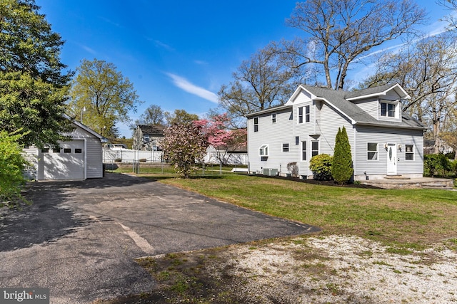 view of side of home featuring driveway, cooling unit, a detached garage, fence, and a yard