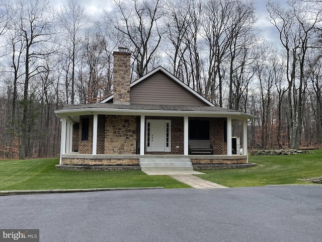 view of front of house featuring brick siding, a porch, a front lawn, and a chimney