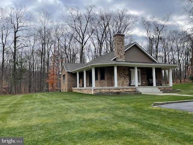 view of front of property with covered porch, a chimney, brick siding, a front lawn, and roof with shingles