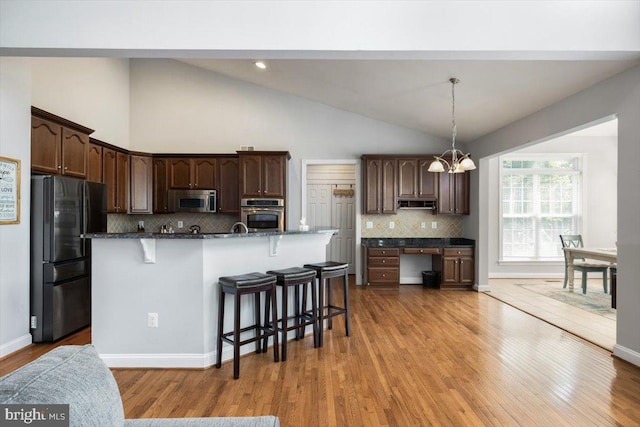 7135 Hills Ln, Warrenton, VA 20187 - kitchen featuring stainless steel appliances, a breakfast bar, dark brown cabinetry, tasteful backsplash, and light wood-style flooring