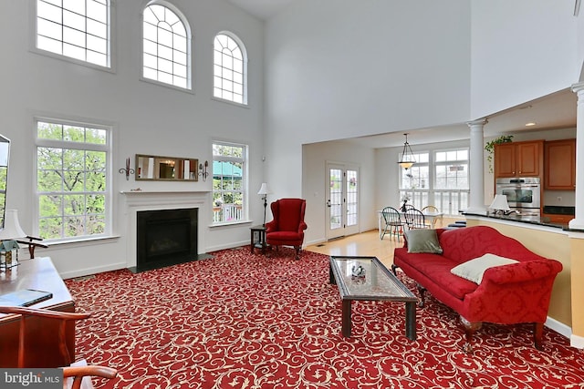 living room with baseboards, a towering ceiling, a fireplace with flush hearth, and a healthy amount of sunlight