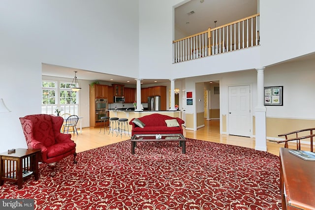 living area featuring light wood finished floors, a high ceiling, and ornate columns