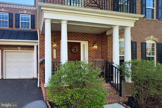 view of exterior entry with a porch, a standing seam roof, a garage, and brick siding