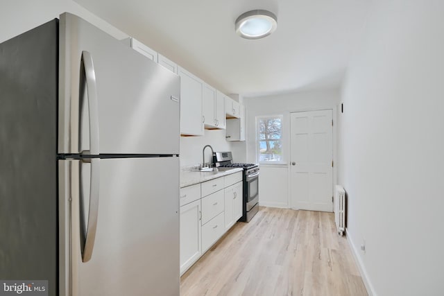 kitchen with white cabinets, light wood-style flooring, light countertops, radiator, and appliances with stainless steel finishes