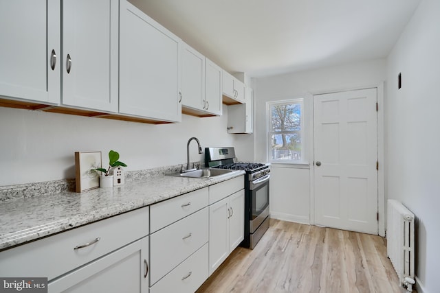 kitchen with light wood-style flooring, a sink, white cabinetry, radiator heating unit, and stainless steel gas stove