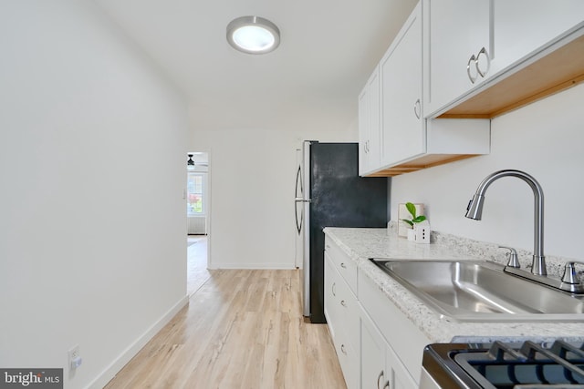 kitchen with white cabinets, light wood finished floors, a sink, freestanding refrigerator, and baseboards