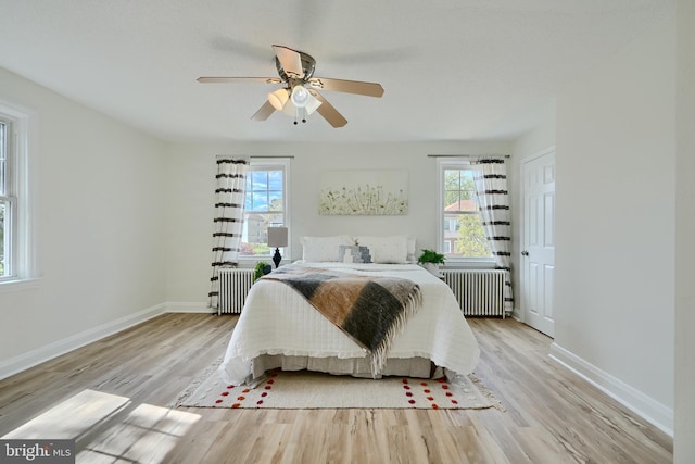 bedroom with radiator heating unit, multiple windows, and light wood finished floors