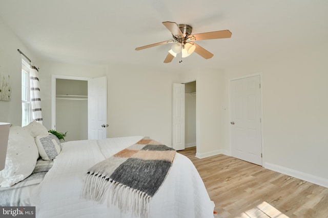 bedroom featuring multiple closets, baseboards, a ceiling fan, and light wood-style floors