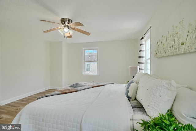 bedroom with baseboards, a ceiling fan, wood finished floors, and multiple windows
