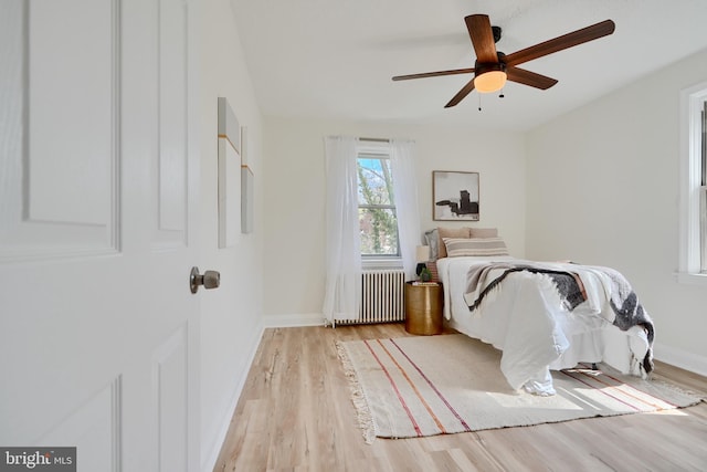 bedroom featuring light wood-style floors, radiator heating unit, baseboards, and ceiling fan