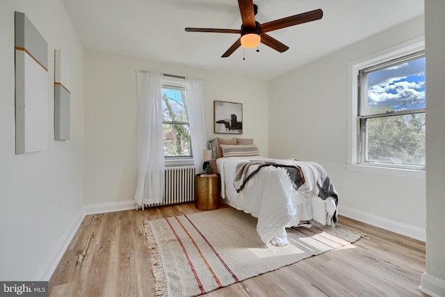 bedroom with radiator, wood finished floors, a ceiling fan, and baseboards