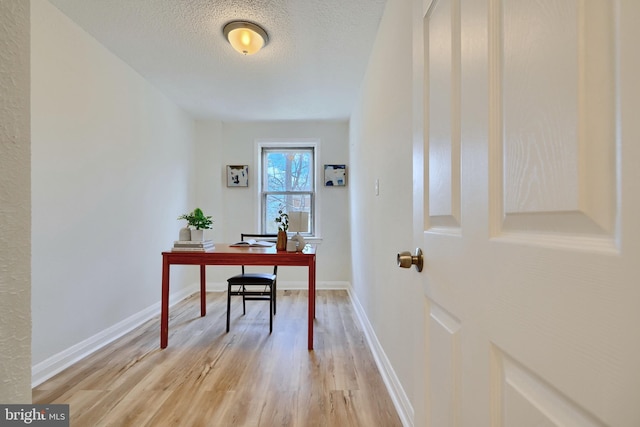 home office with light wood finished floors, baseboards, and a textured ceiling