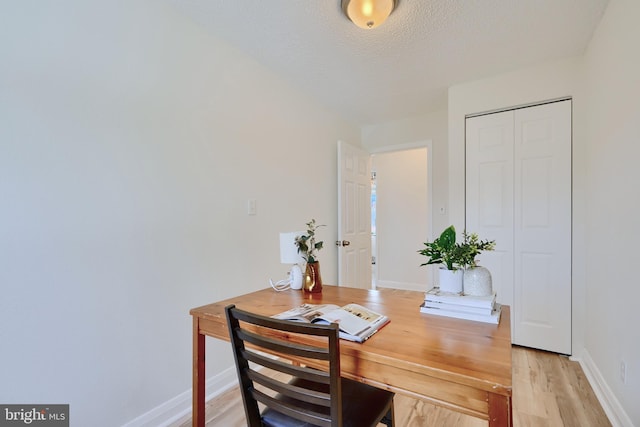 office space featuring light wood finished floors, baseboards, and a textured ceiling