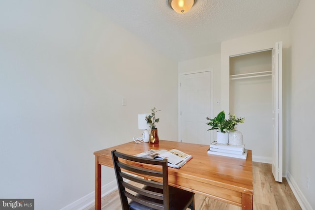 home office with light wood-style floors, a textured ceiling, and baseboards