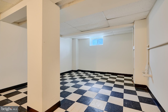 basement featuring tile patterned floors, a paneled ceiling, and baseboards