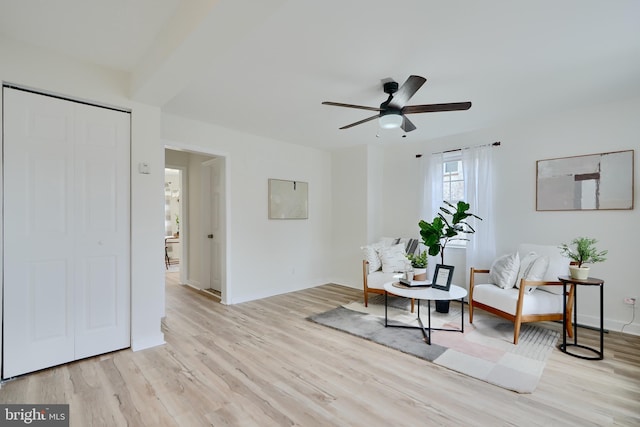 living area featuring baseboards, a ceiling fan, and light wood-style flooring