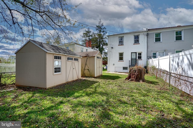 rear view of property featuring a lawn, a fenced backyard, an outbuilding, and a shed