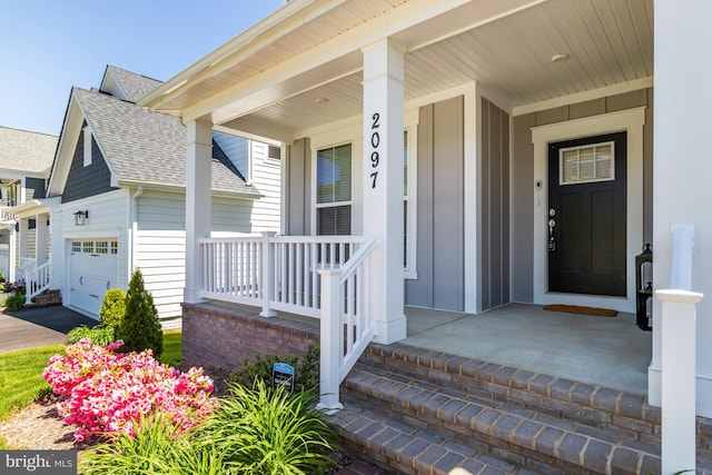 view of exterior entry with covered porch, board and batten siding, a shingled roof, and a garage