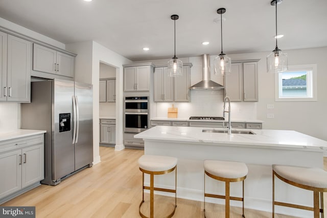kitchen featuring appliances with stainless steel finishes, a sink, wall chimney exhaust hood, tasteful backsplash, and gray cabinetry