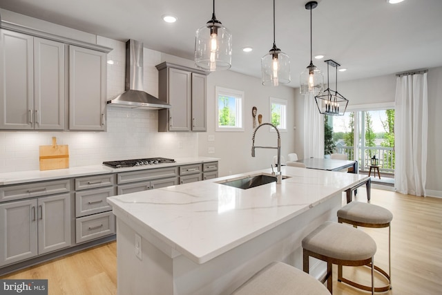 kitchen featuring decorative backsplash, gray cabinetry, a sink, light wood finished floors, and wall chimney exhaust hood