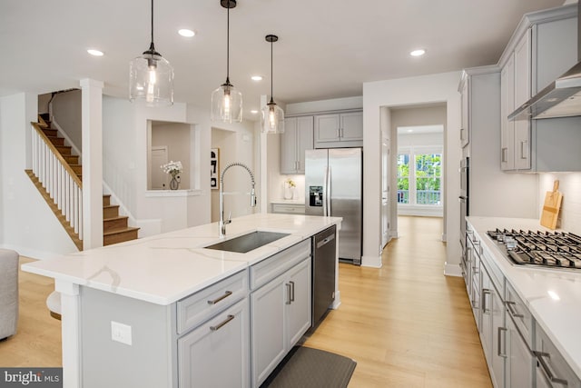 kitchen with a sink, appliances with stainless steel finishes, gray cabinets, and wall chimney exhaust hood