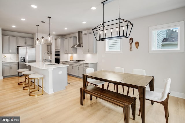 kitchen featuring a breakfast bar area, light wood-type flooring, wall chimney exhaust hood, appliances with stainless steel finishes, and gray cabinetry