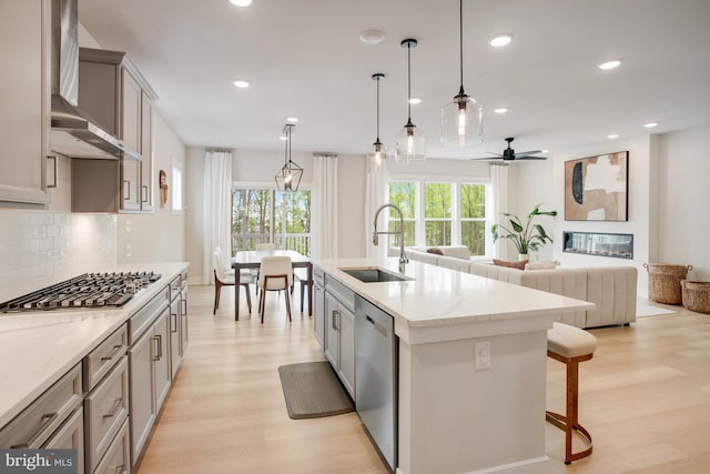 kitchen featuring wall chimney exhaust hood, a sink, light wood-style flooring, backsplash, and stainless steel appliances