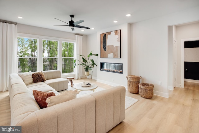 living room with ceiling fan, a glass covered fireplace, light wood-style flooring, recessed lighting, and baseboards