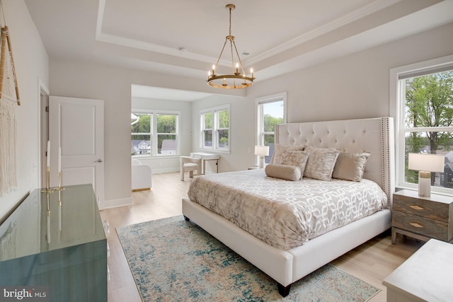 bedroom with an inviting chandelier, a raised ceiling, crown molding, and light wood-style flooring