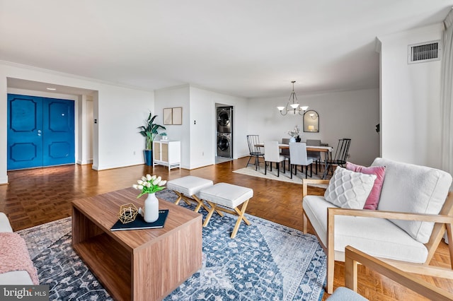 living area featuring stacked washer / dryer, a chandelier, and baseboards