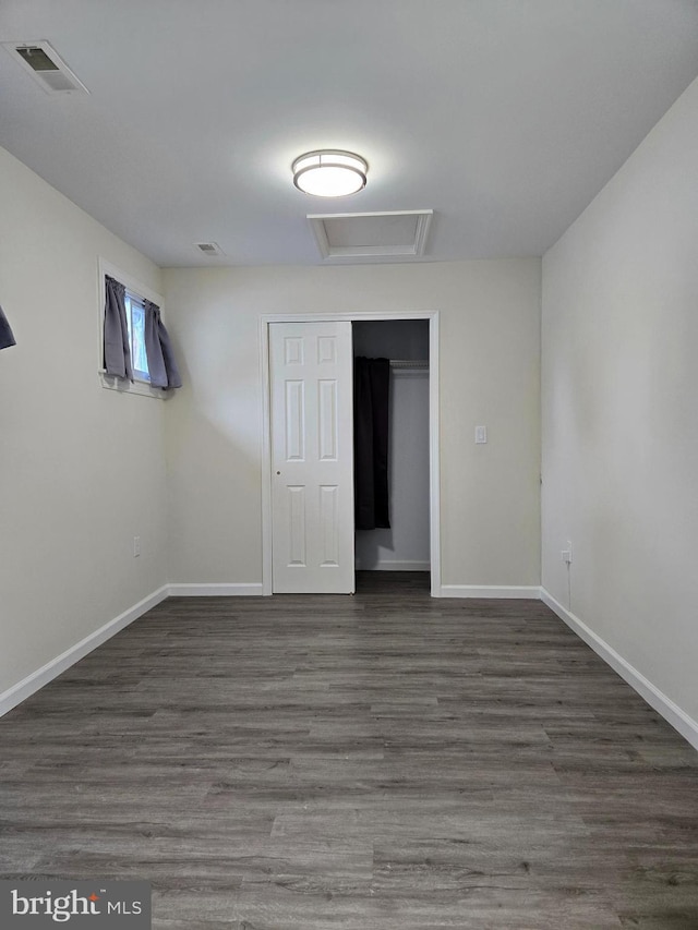 empty room featuring wood finished floors, attic access, baseboards, and visible vents