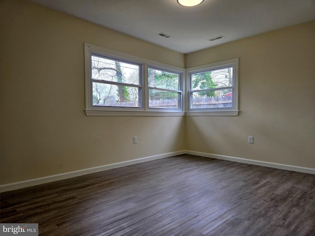 spare room featuring visible vents, baseboards, and dark wood-style floors